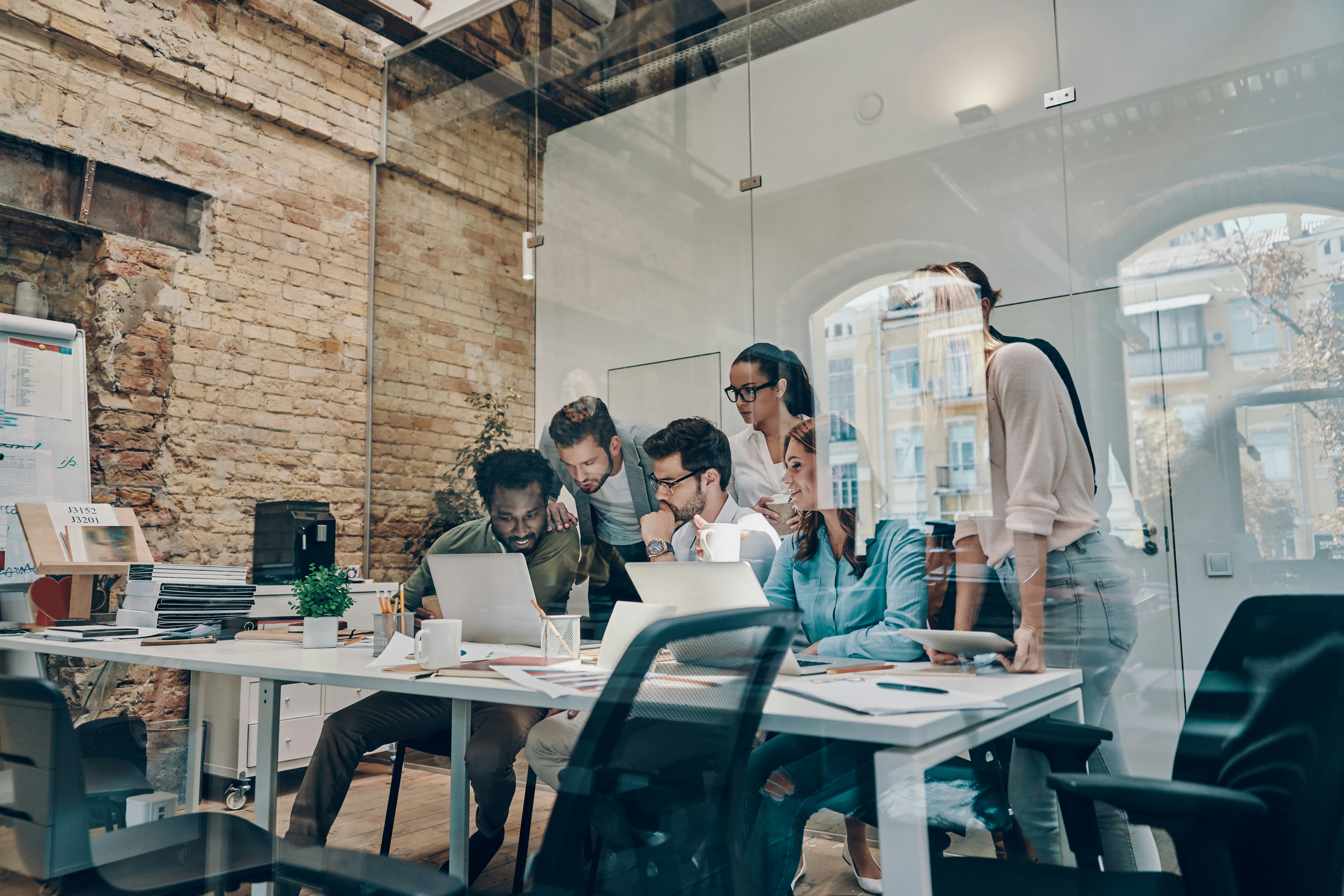A team collaborating around laptops in a modern glass-walled office